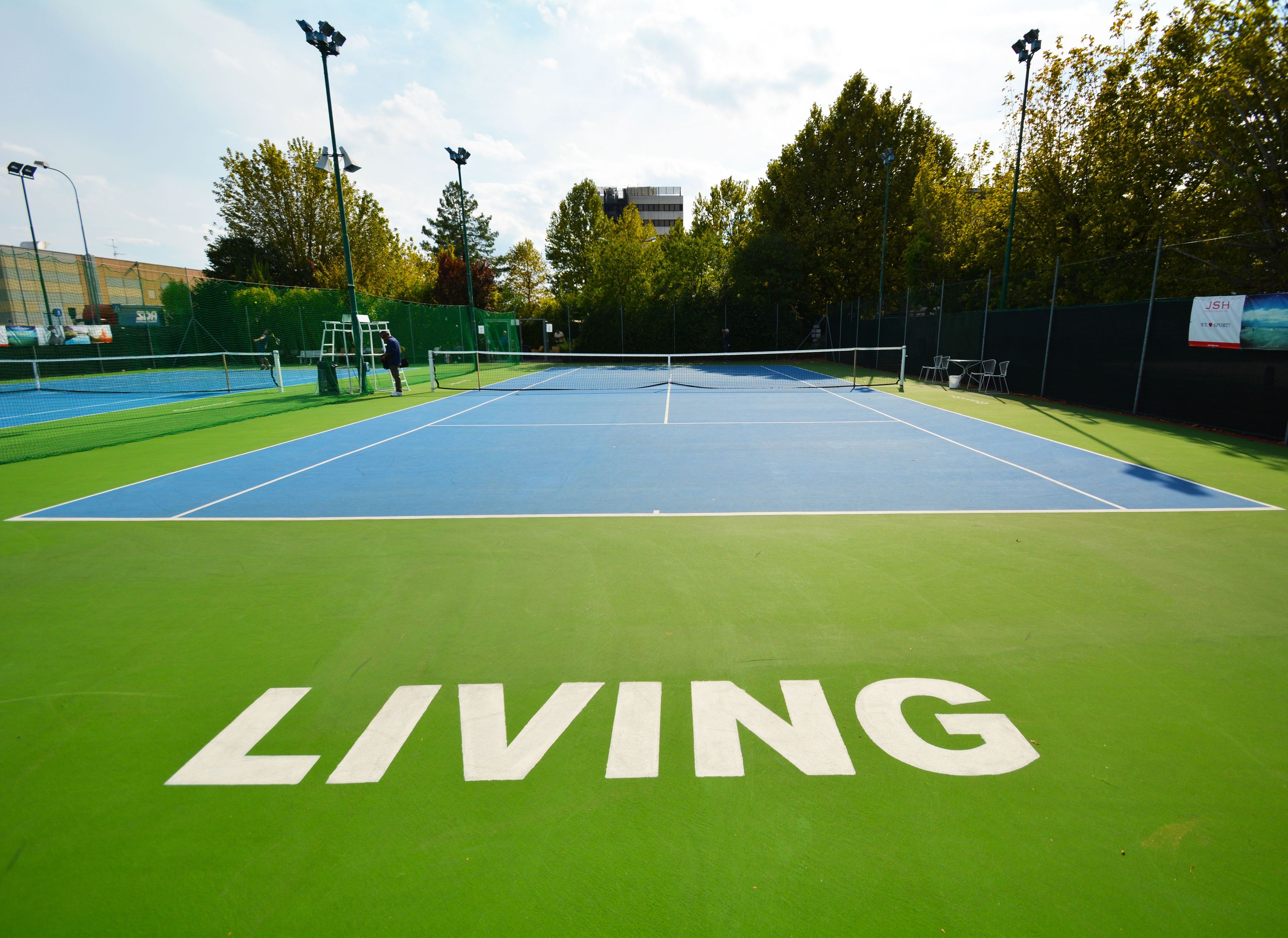 Una cancha de tenis al aire libre con superficie verde y la palabra 'LIVING' pintada.