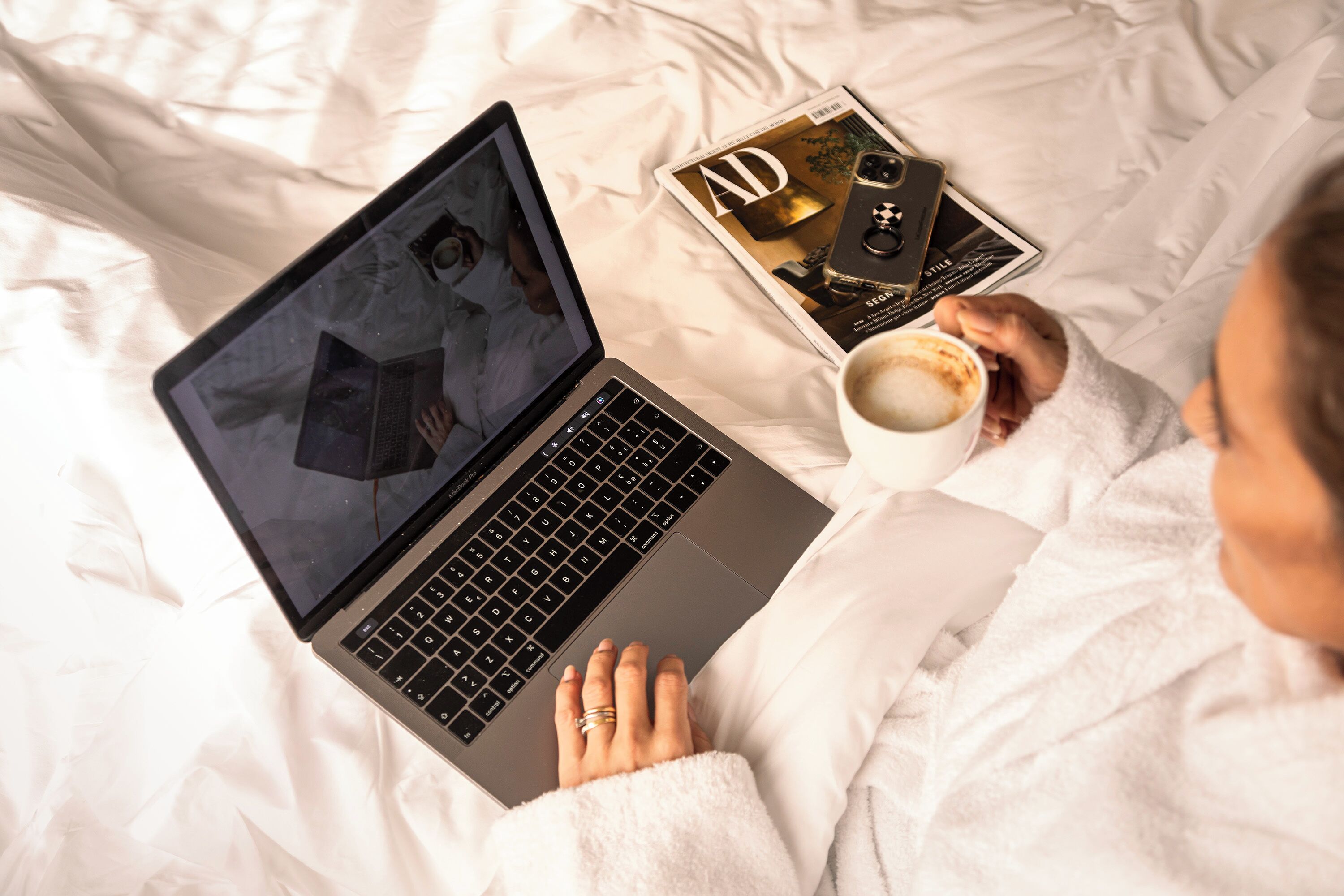 A person lying on a bed with a laptop, a magazine, and a cup of coffee.