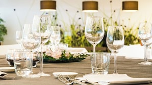 A dining table set with multiple wine glasses, plates, and cutlery, with a floral centerpiece and pendant lights in the background. - Living Place Hotel (Bologna)