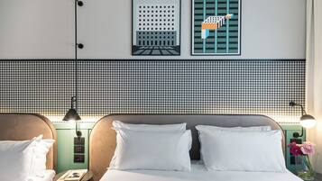 Camera d'albergo con una testiera a motivi a caccia, due letti con lenzuola bianche, un comodino con lampada e un punto luce a parete.
