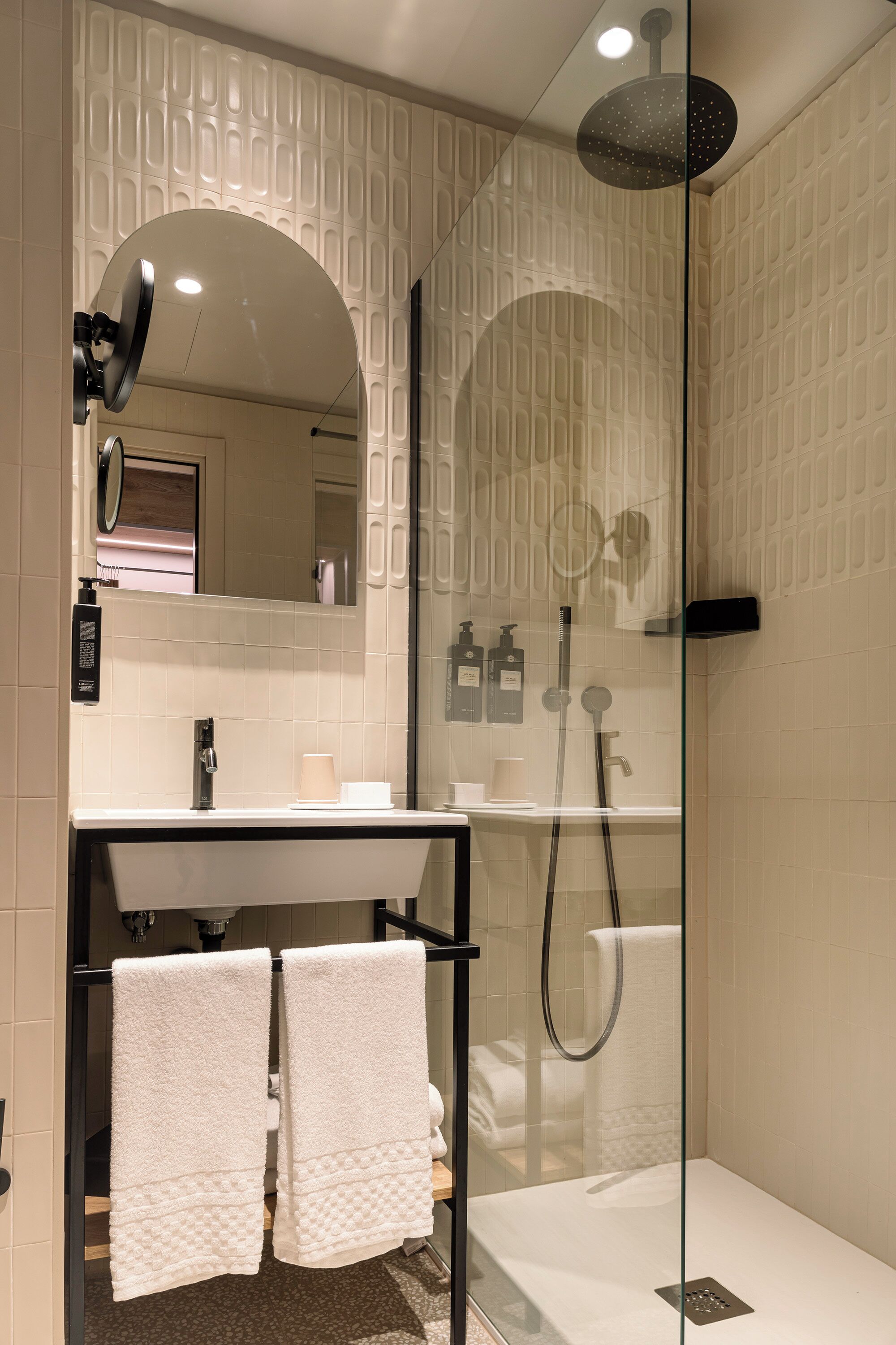 Un bagno moderno con cabina doccia in vetro, un mobile lavabo con specchio e due asciugamani su un porta-asciugamani.
