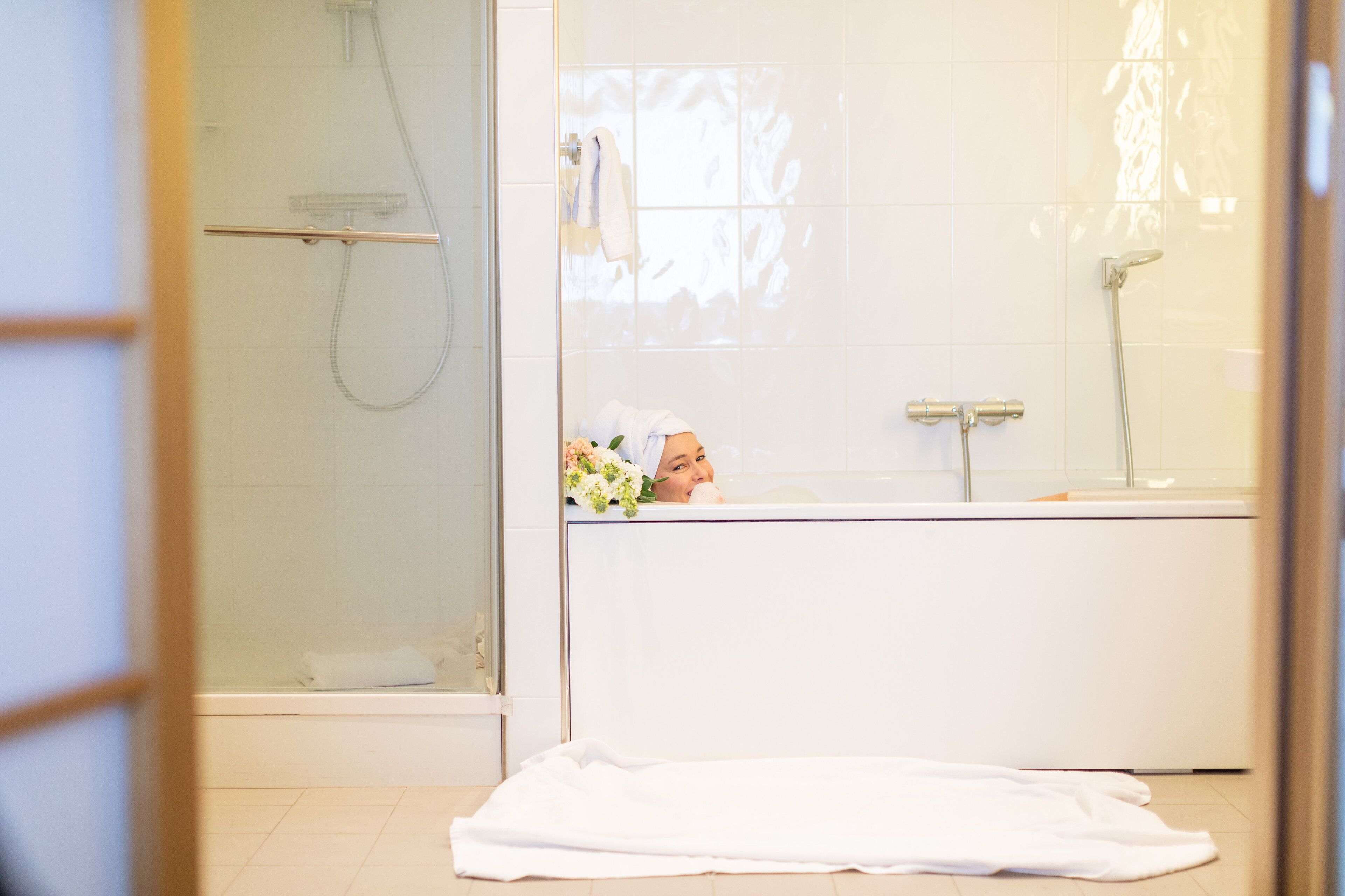 A bathroom with a glass shower enclosure, a bathtub, and a window with a towel hanging on the wall.