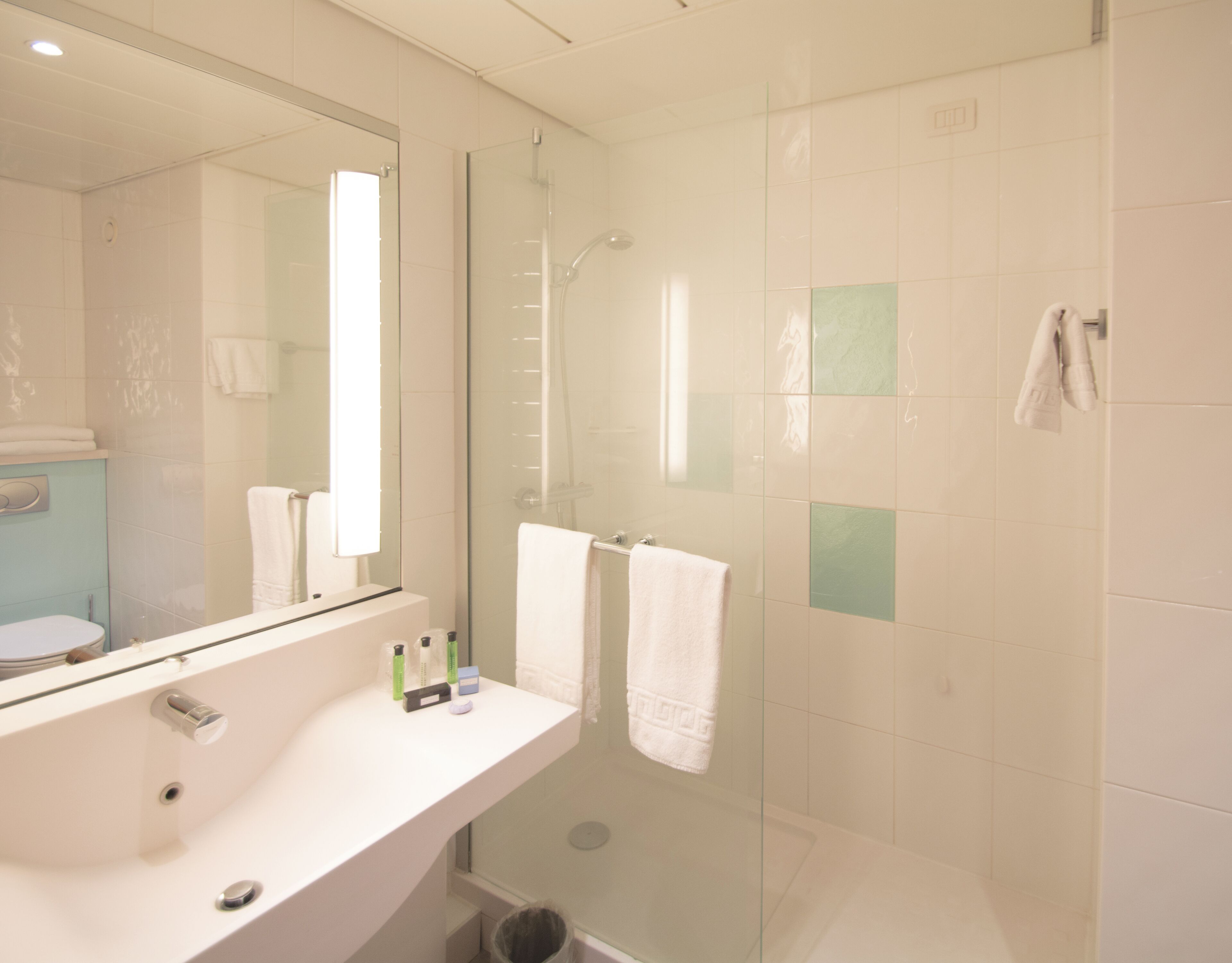 Un baño moderno con cabina de ducha de vidrio, lavabo blanco y un espejo grande.
