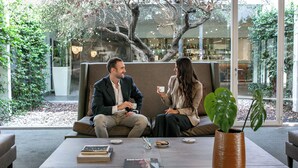 Two people sitting on a couch in a modern indoor space with a coffee table, books, and a potted plant. - Living Place Hotel (Bologna)