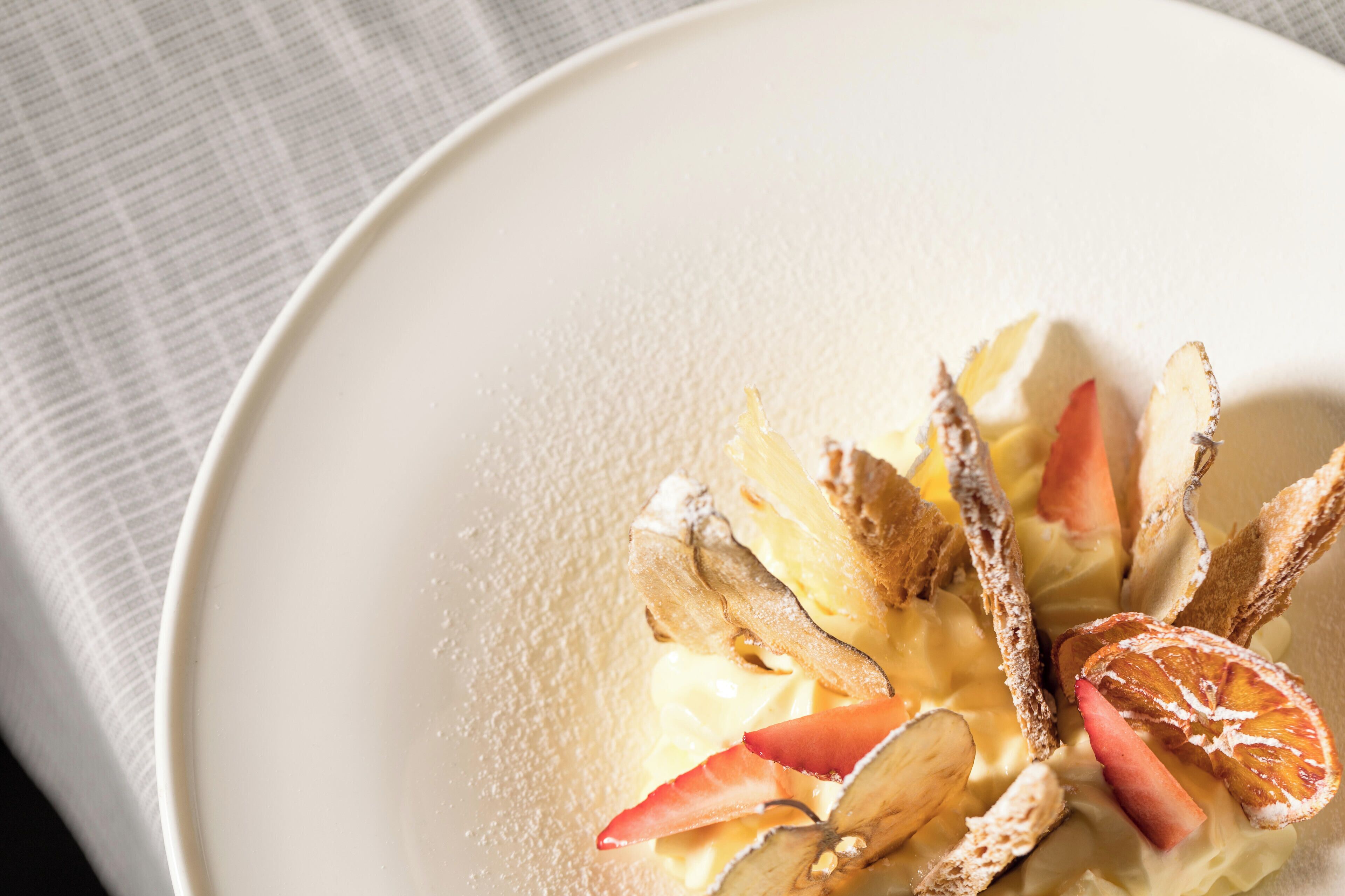A white plate with a dessert consisting of sliced fruits and a powdered topping.