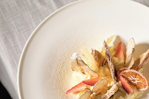 Een wit bord met een dessert van gesneden fruit en een poedersuikerlaag.