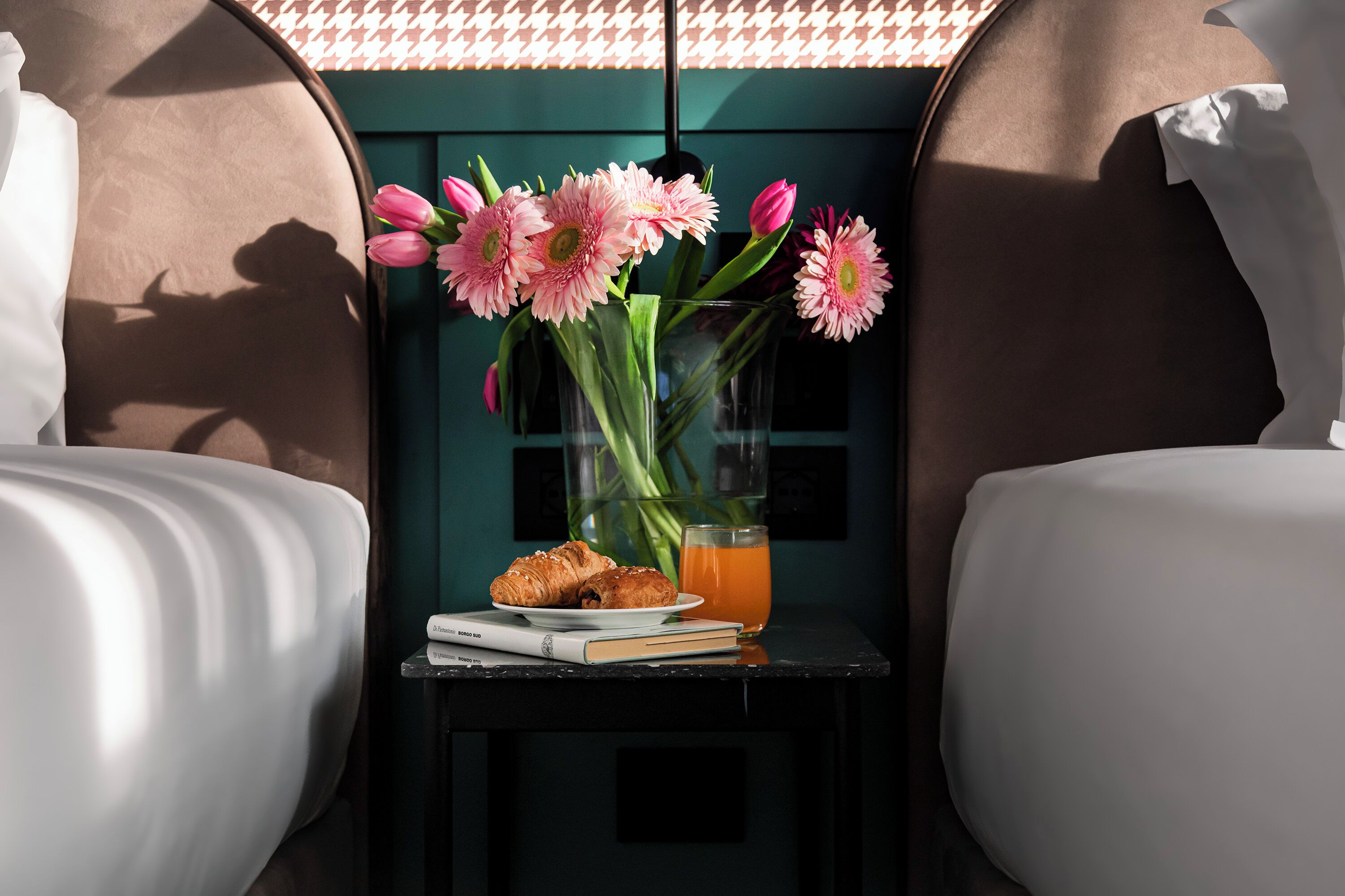 A small table with a vase of pink flowers, a glass of orange juice, and a plate of croissants.