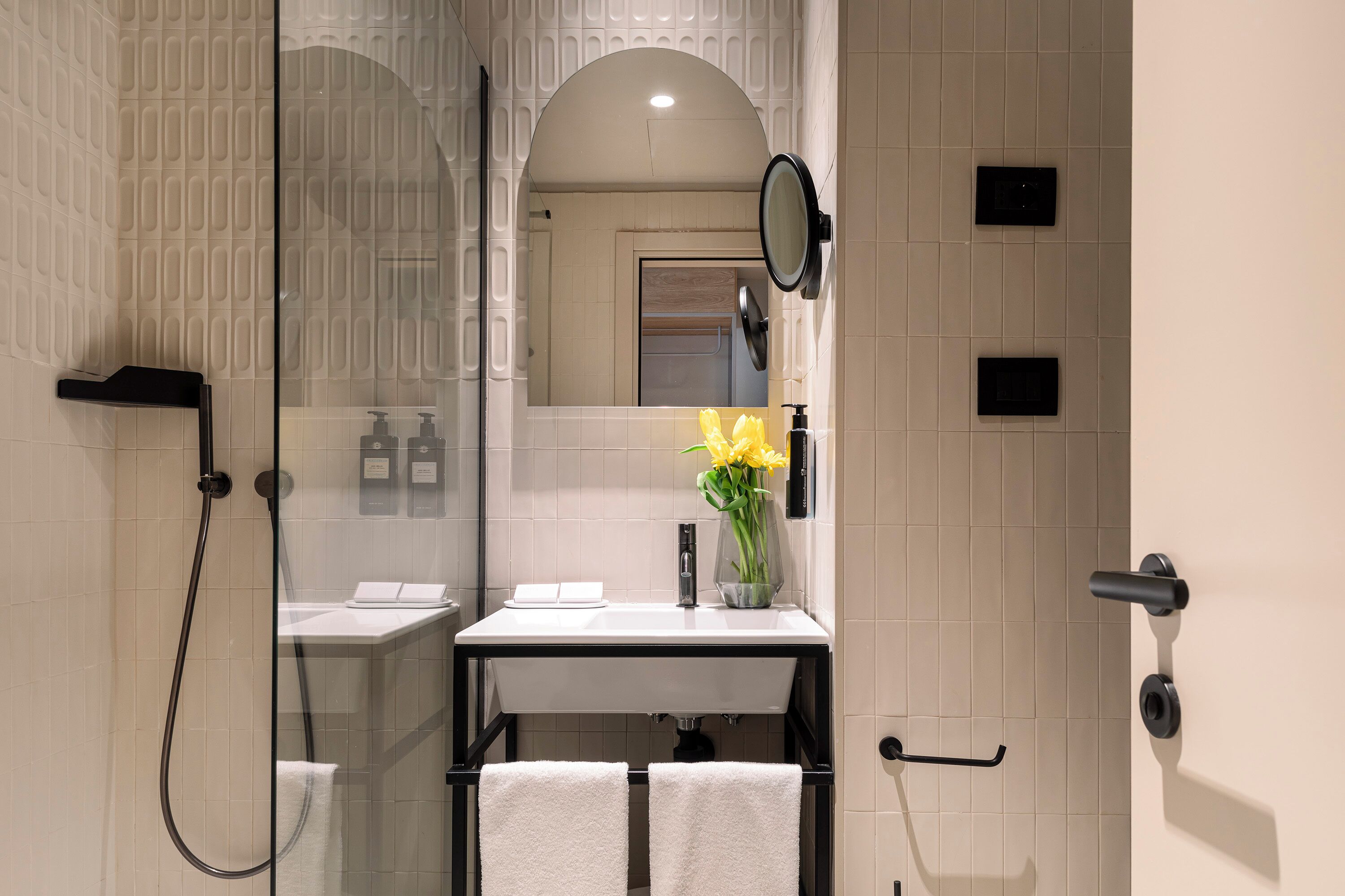 A modern bathroom with a glass shower enclosure, a white sink with a black faucet, and a mirror above the sink.