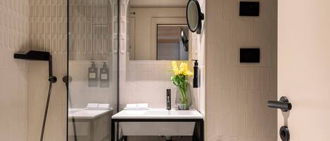 A modern bathroom with a glass shower enclosure, a white sink with a black faucet, and a mirror above the sink.
