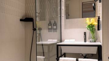 A modern bathroom with a glass-enclosed shower, a white sink with a vase of flowers, and a black towel rack.