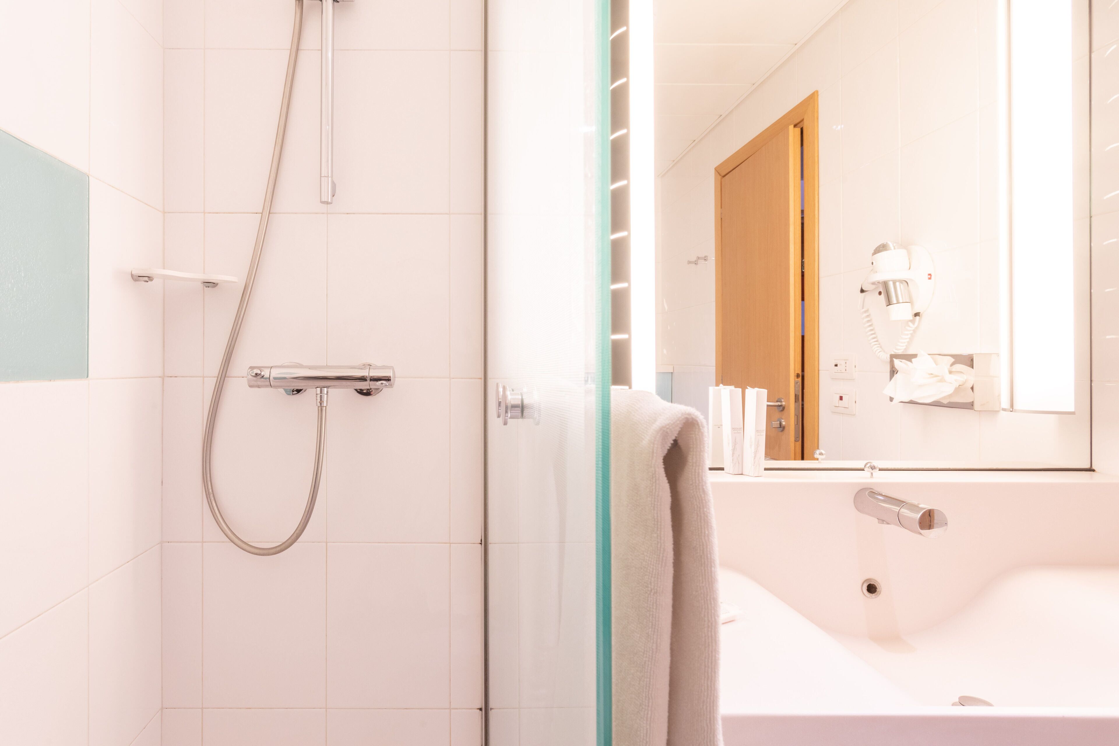 A modern bathroom with a glass shower enclosure, a white sink, and a mirror reflecting a door and a hairdryer.