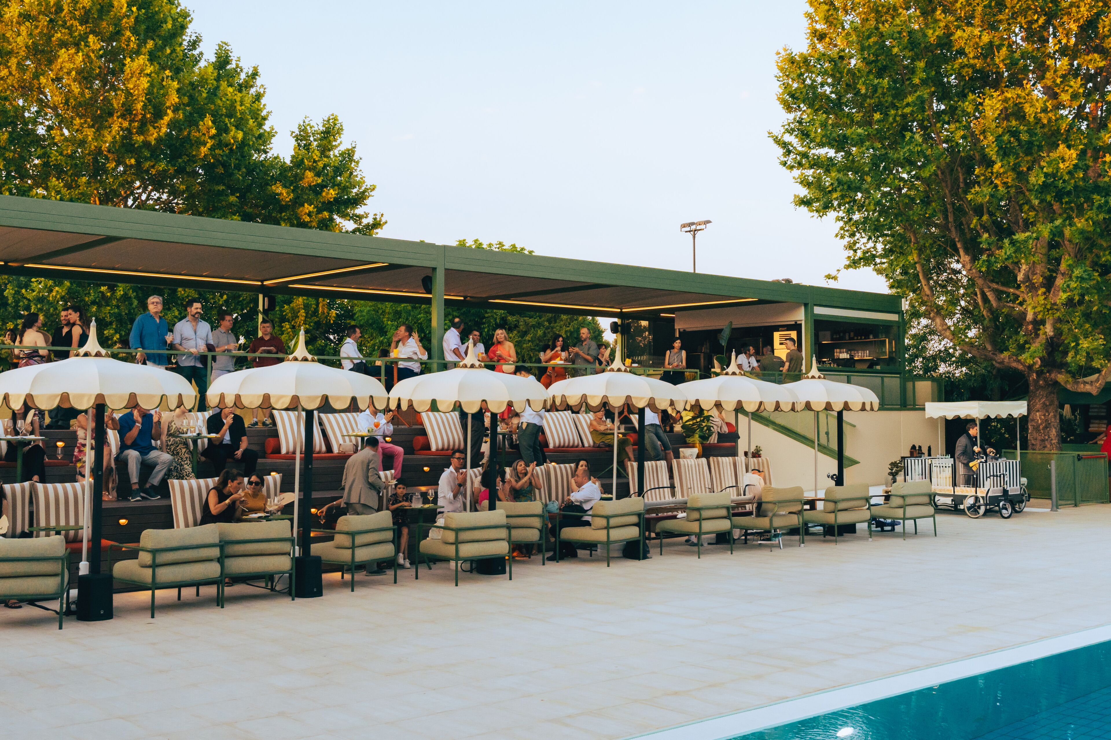 Un'area salotto esterna con ombrelloni e sedie, una piscina e una galleria coperta.