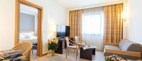 A hotel room with a bed, a desk with a computer, two chairs, a sofa, and a TV.