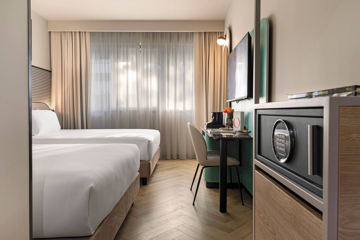 Ein Hotelzimmer mit zwei Betten, einem Schreibtisch mit Computer und einer Minibar.