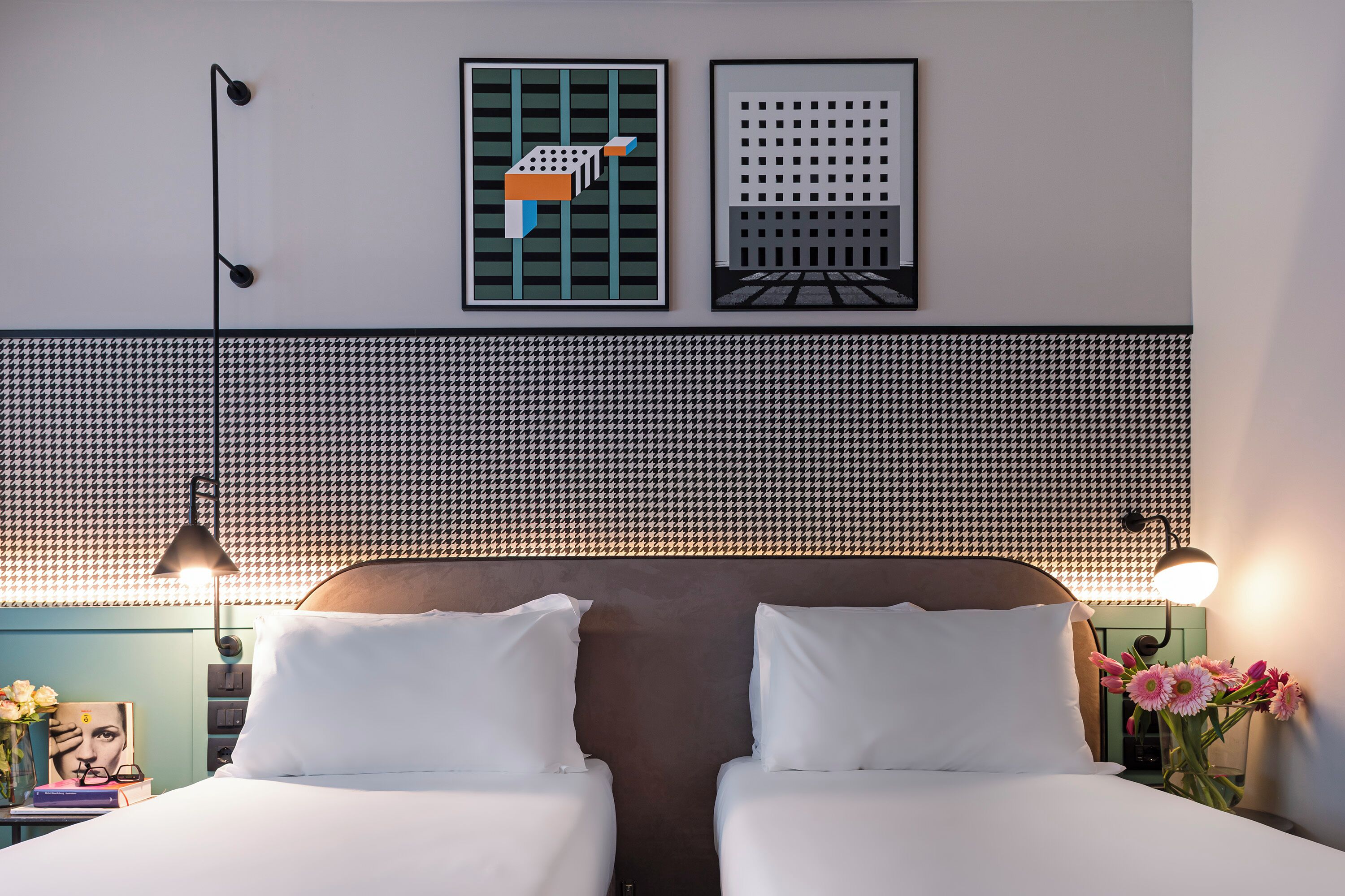 A hotel room with two beds, a houndstooth-patterned headboard, wall-mounted artwork, and bedside lamps.