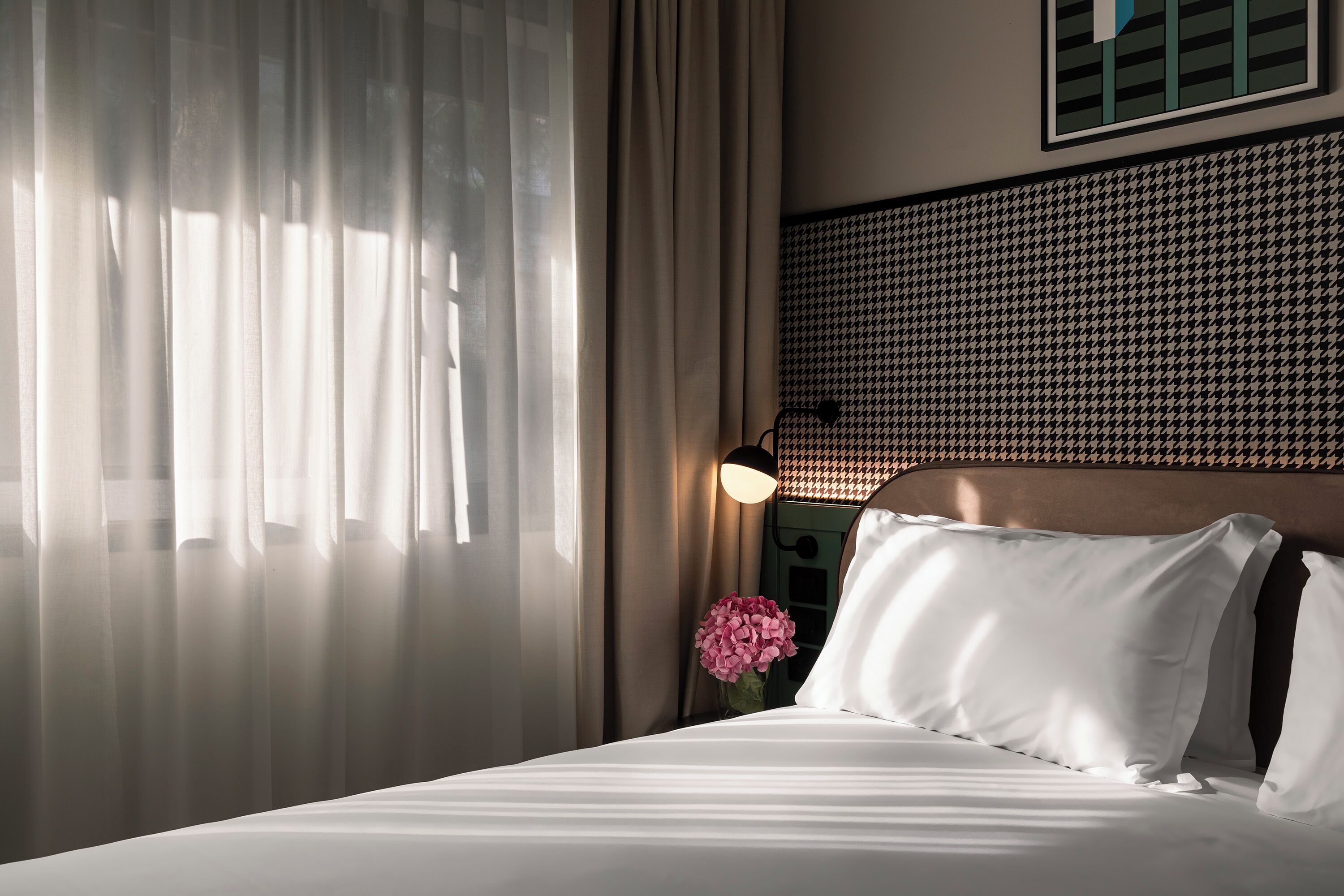 Een hotelkamer met een bed, gordijnen, een lamp en een gestreept hoofdeinde.