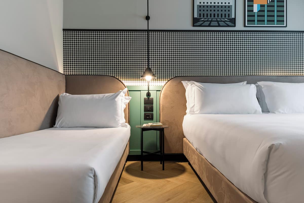 Ein Hotelzimmer mit zwei Betten, einem kleinen Tisch, einer grünen Wand und einem gemusterten Kopfteil.