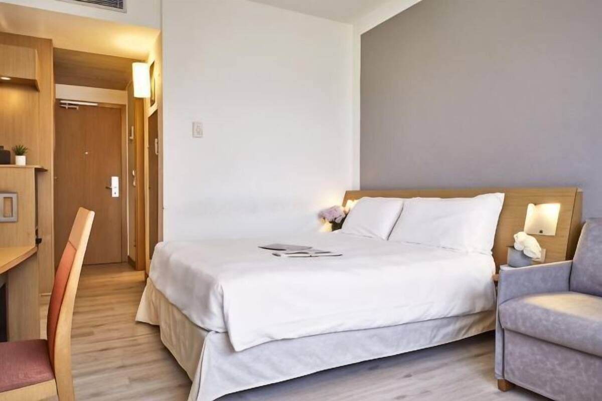 Ein Hotelzimmer mit einem Bett, einem Schreibtisch, einem Stuhl und einem kleinen Tisch mit einer Lampe.