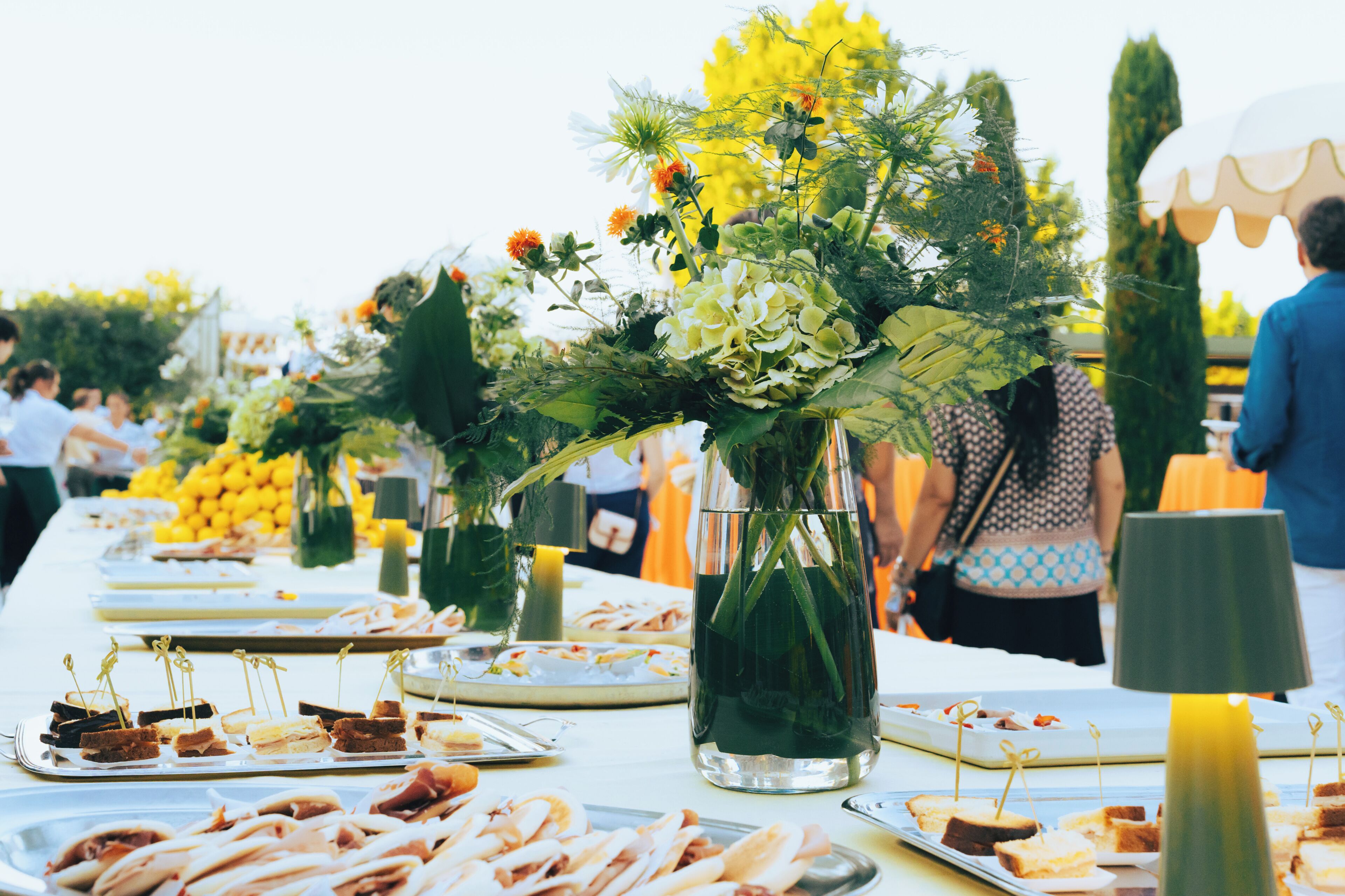 A buffet table with various food items and floral centerpieces.