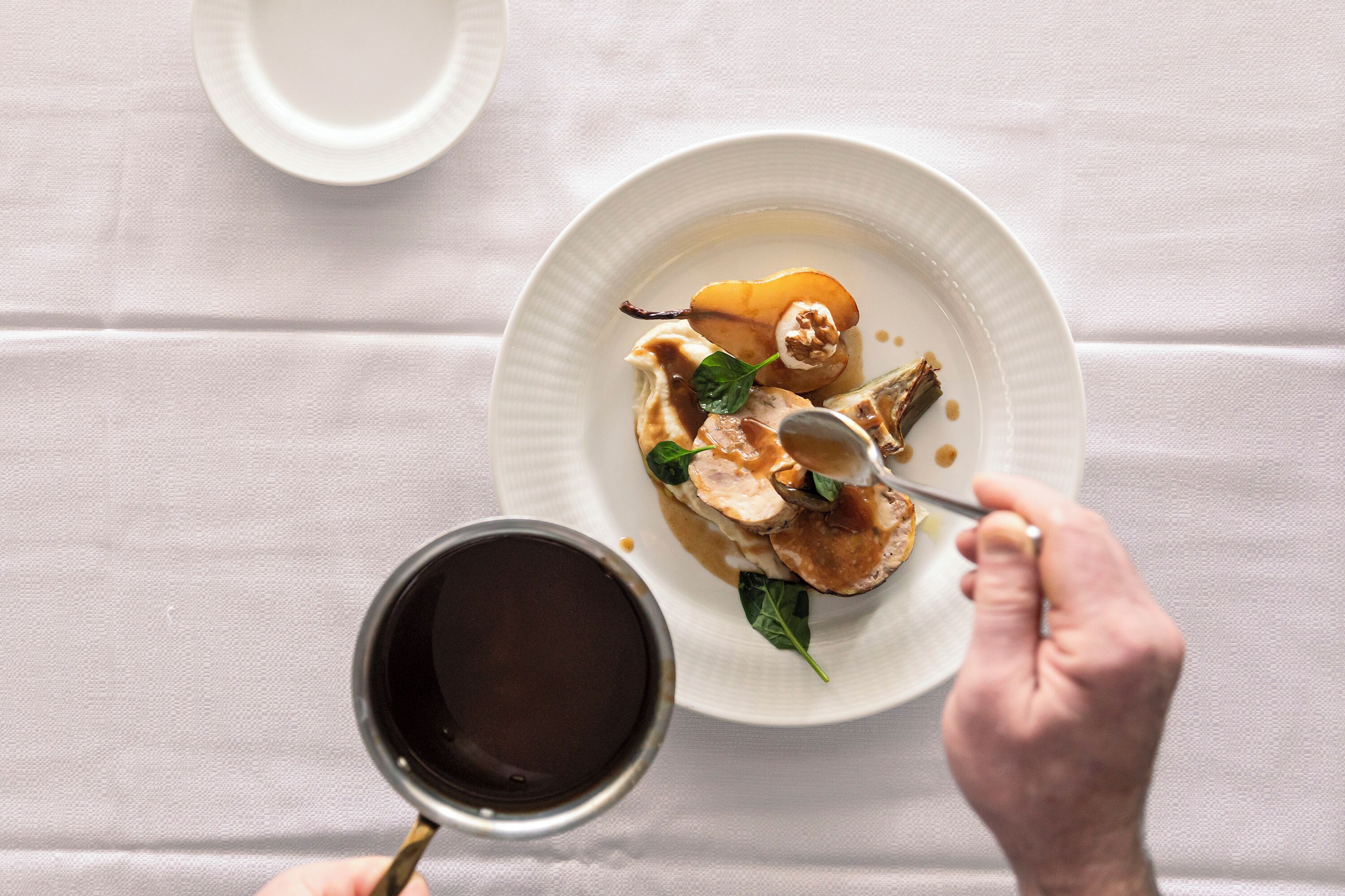 A white plate with a dessert, a spoon, and a cup of coffee on a white tablecloth.