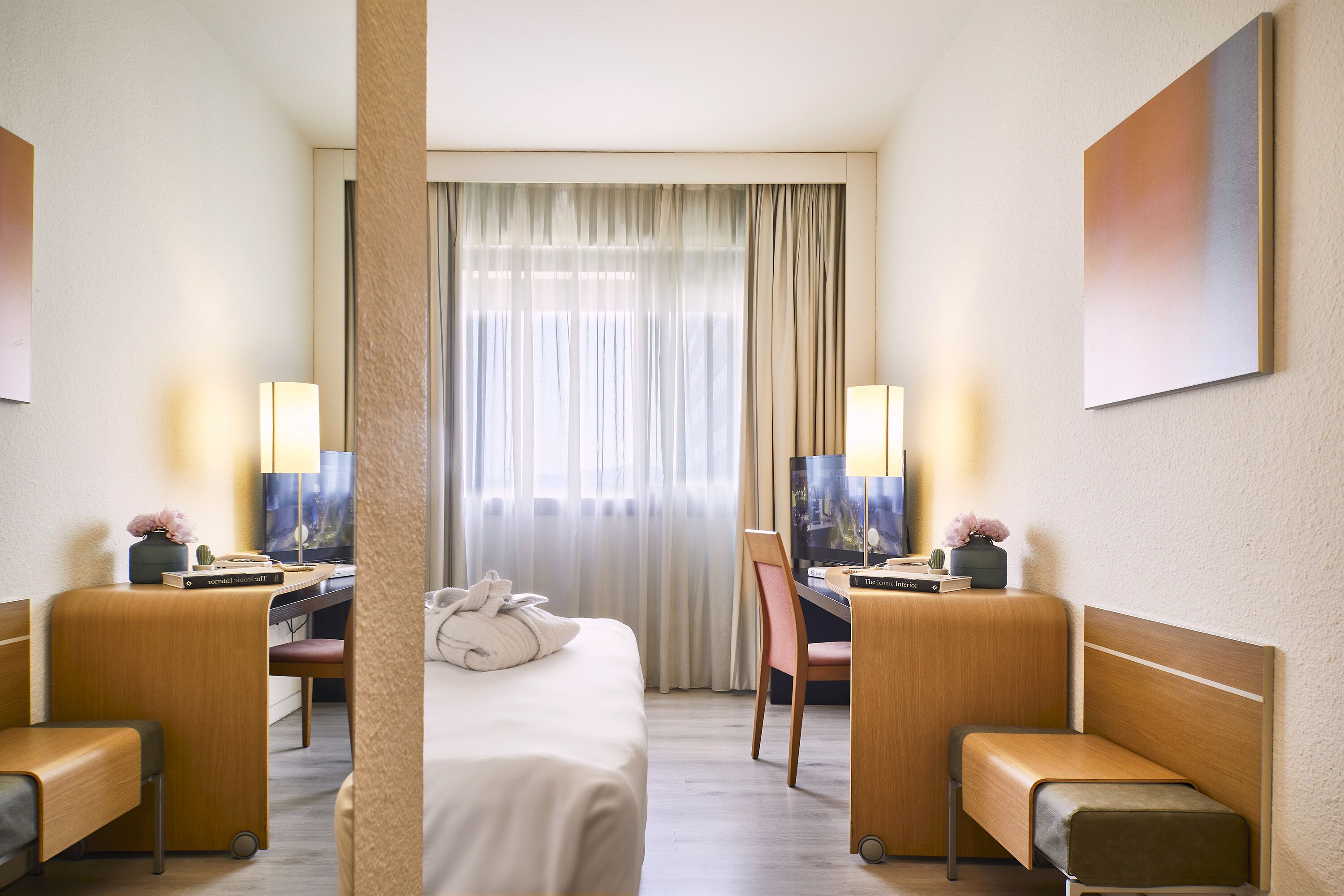 A hotel room with a bed, two chairs, a desk, a television, and a window with curtains.