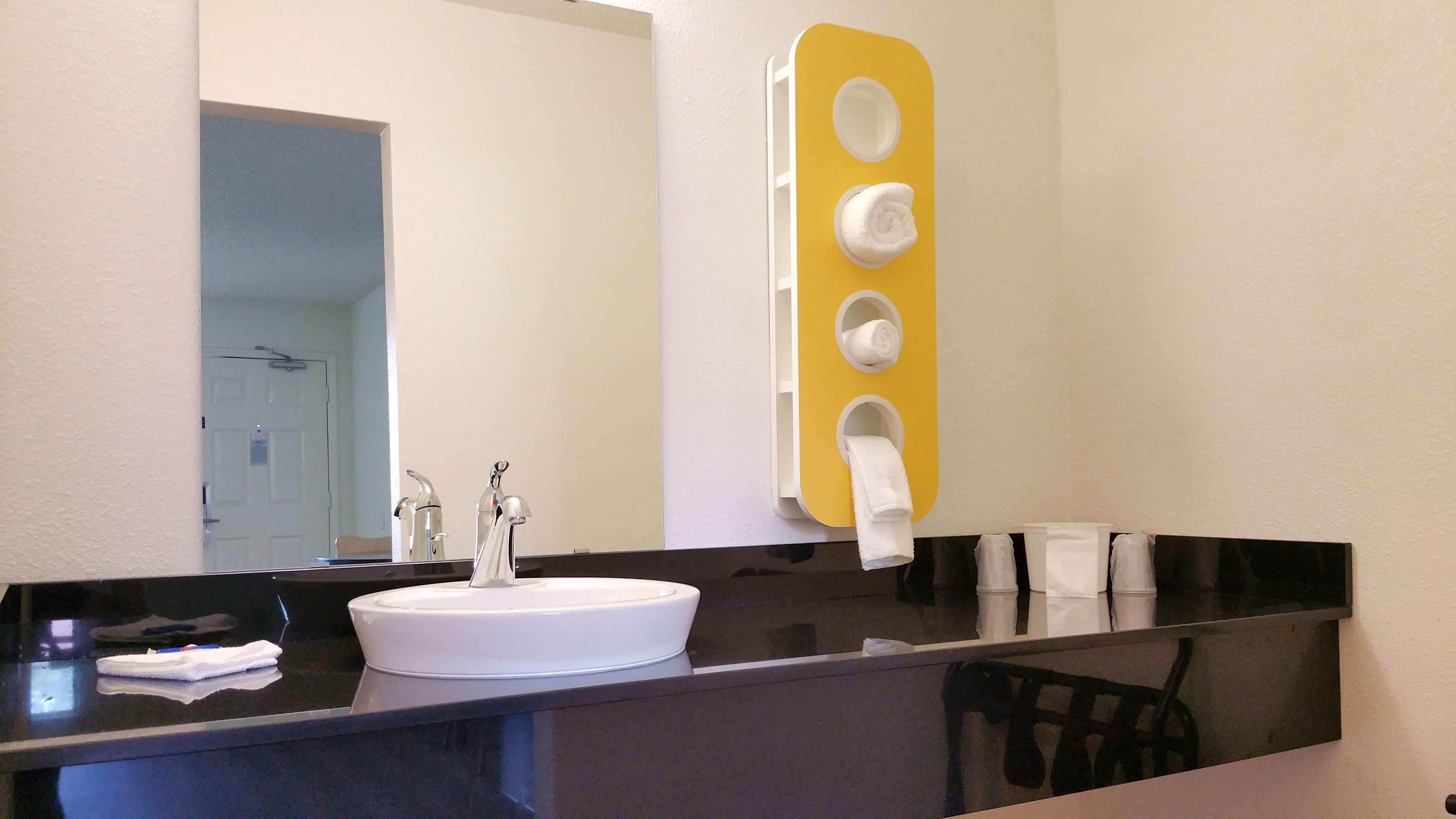 A bathroom with a white sink, a mirror, and a yellow soap dispenser wall.