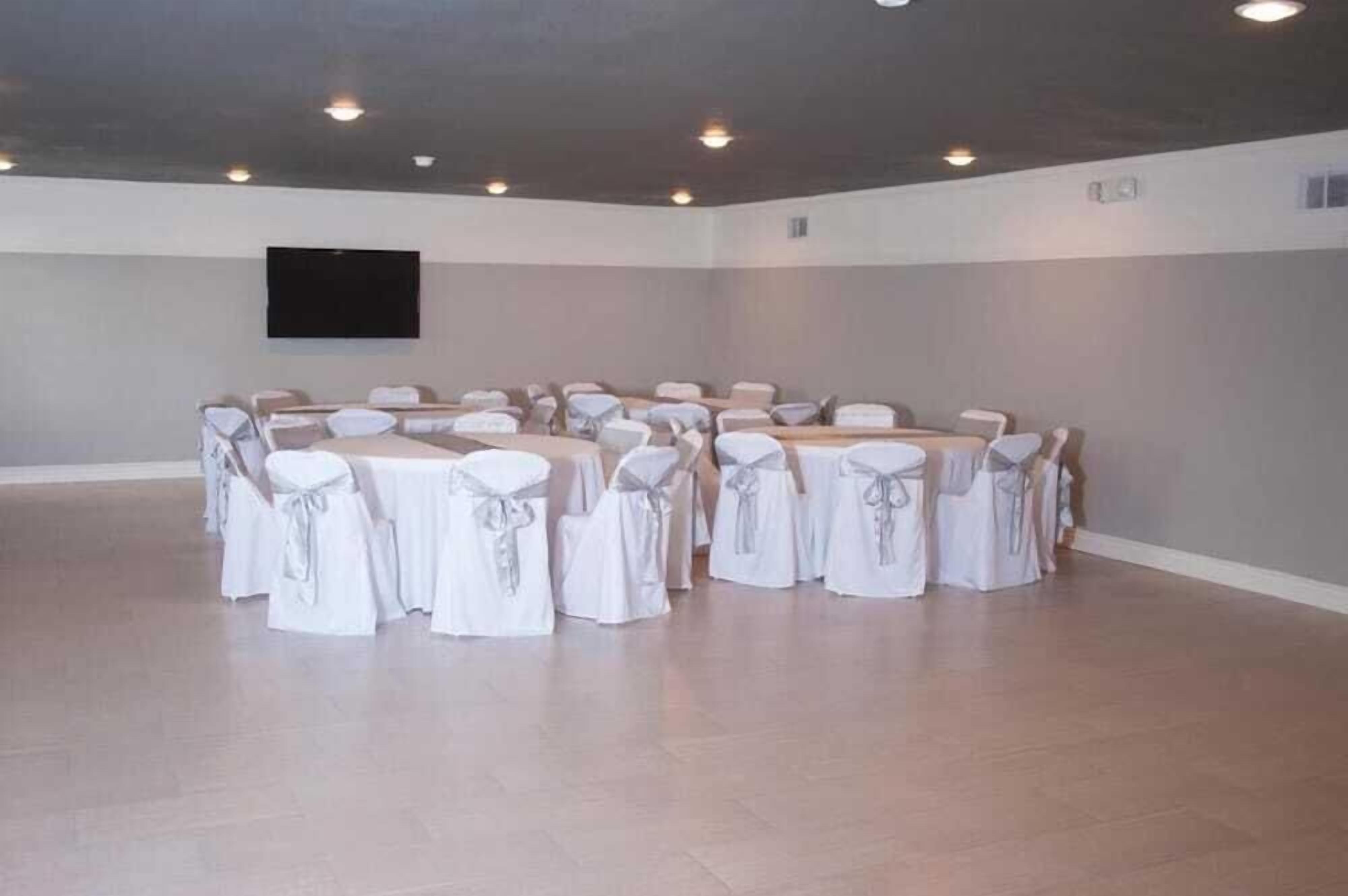 A conference room with round tables and chairs, a flat-screen TV mounted on the wall, and a neutral color scheme.