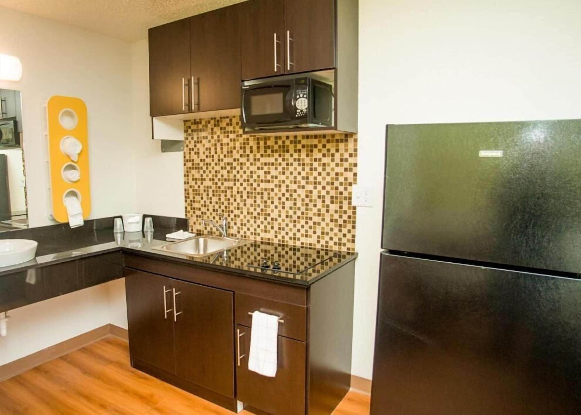 Uma cozinha compacta com armários de madeira escura, micro-ondas, geladeira e painel de azulejos.