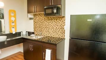 Uma cozinha compacta com armários de madeira escura, micro-ondas, geladeira e painel de azulejos.