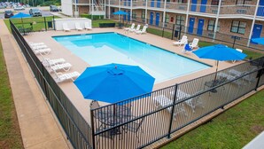 A swimming pool with lounge chairs and umbrellas, surrounded by a fence, with a building in the background. - Motel 6 Palestine, TX (Palestine)