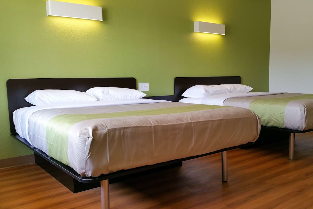 Two single beds with wooden frames and white bedding, a green wall, and two wall-mounted light fixtures.