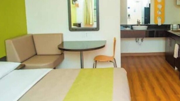 A compact hotel room with a bed, a small round table, a chair, a kitchenette, and a mirror. - Motel 6 Palestine, TX (Palestine)