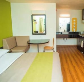 A compact hotel room with a bed, a small round table, a chair, a kitchenette, and a mirror. - Motel 6 Palestine, TX (Palestine)