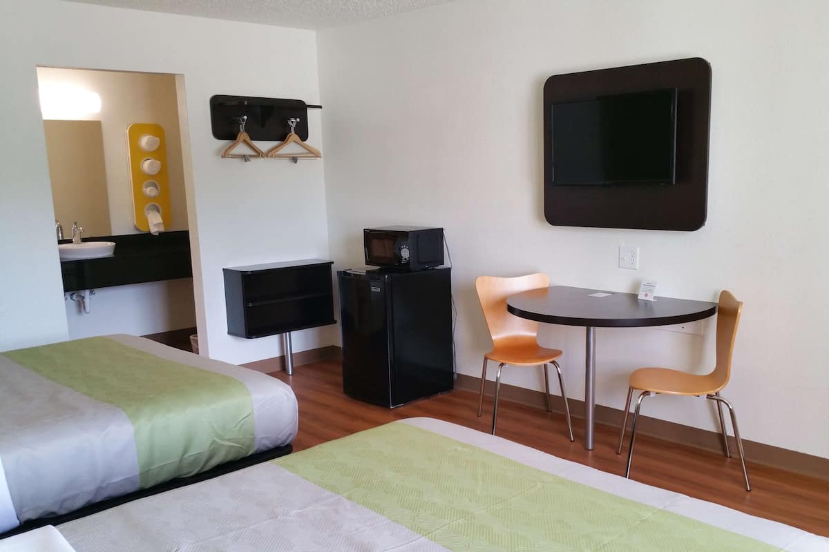 A hotel room with two beds, a desk with a chair, a TV, and a small refrigerator.