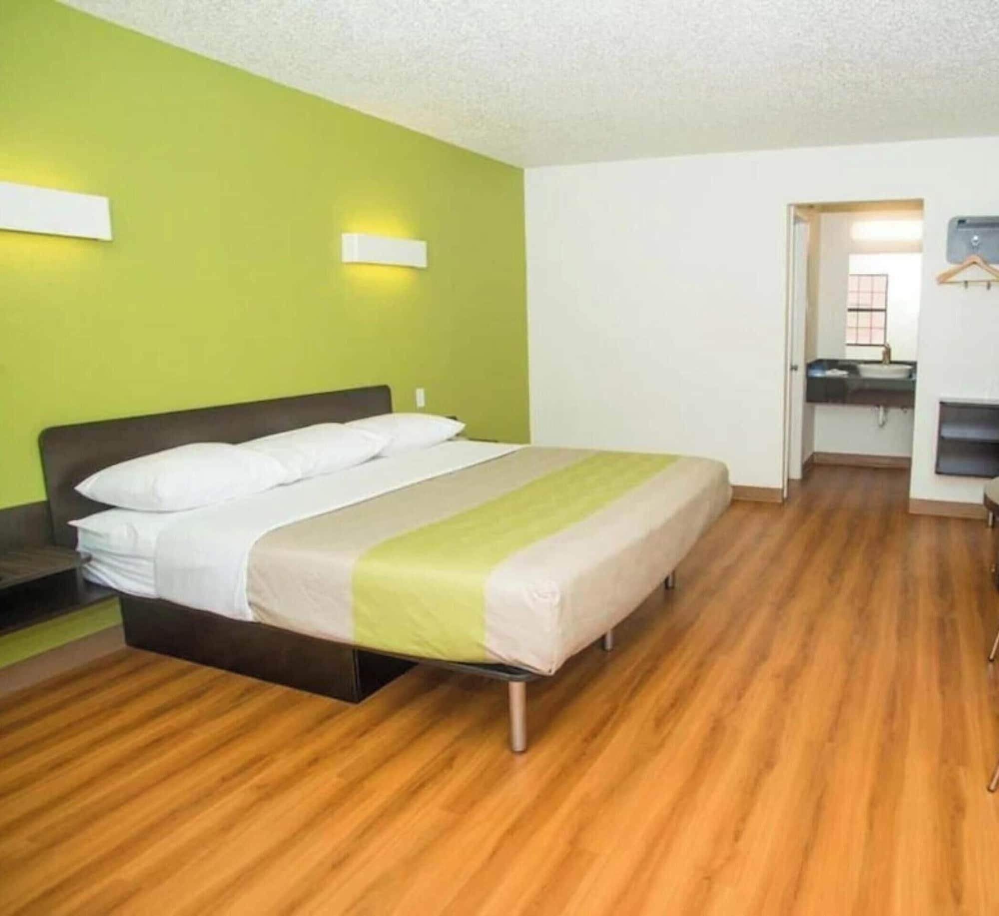 Habitación de hotel con cama, escritorio y baño visible a través de una puerta abierta.
