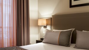 Une chambre d’hôtel avec un lit, des oreillers, une table de chevet, une lampe et une fenêtre avec des rideaux.
