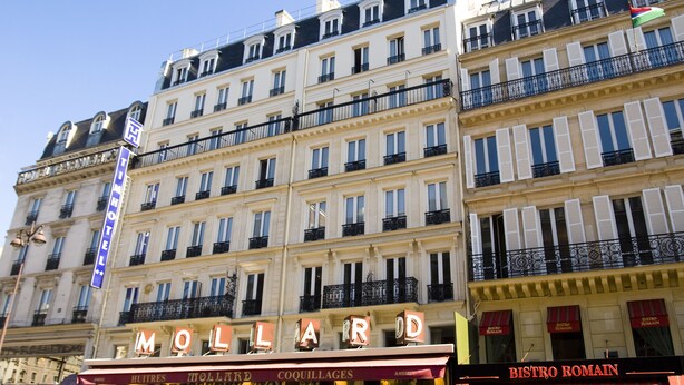 Un hôtel à plusieurs étages, doté de balcons et d’une enseigne indiquant « MOLLARD » et « BISTRO ROMAIN ».