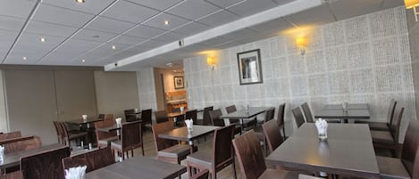 Un restaurant avec plusieurs tables et chaises, un mur décoré de motifs et des luminaires au plafond.