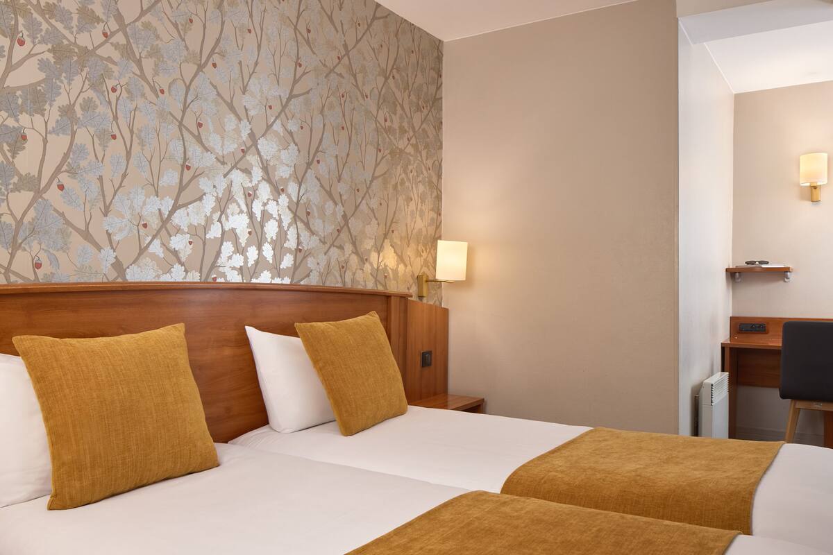 A hotel room with a large bed, two pillows, a nightstand, a lamp, a desk, and a chair.