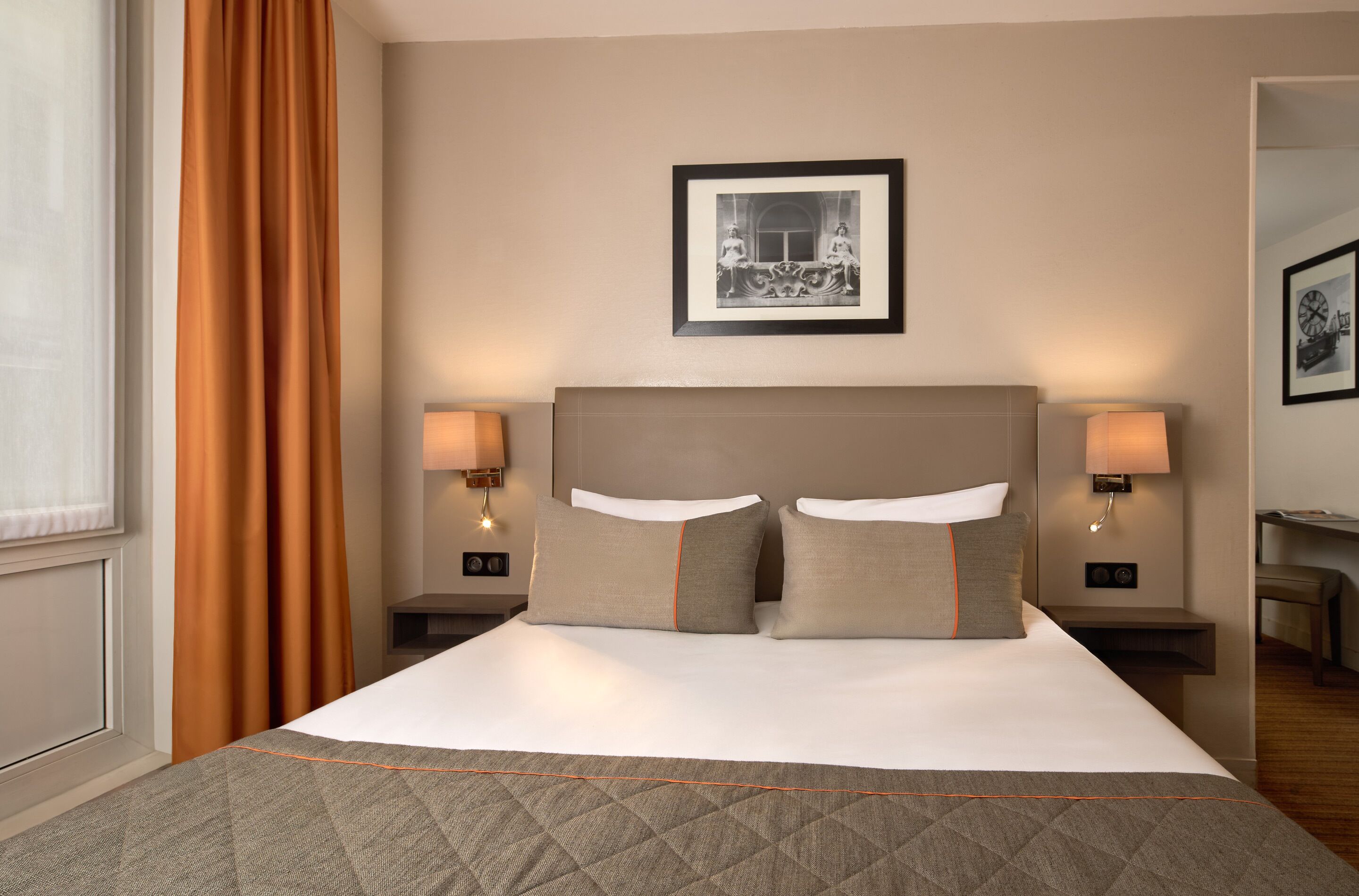 A hotel room with a large bed, two bedside tables with lamps, a framed picture on the wall, and a window with curtains.