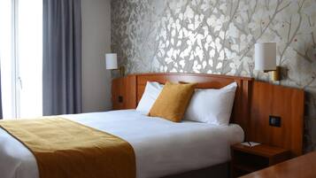 Una camera d'albergo con un letto, un comodino, una lampada e una finestra con tende.