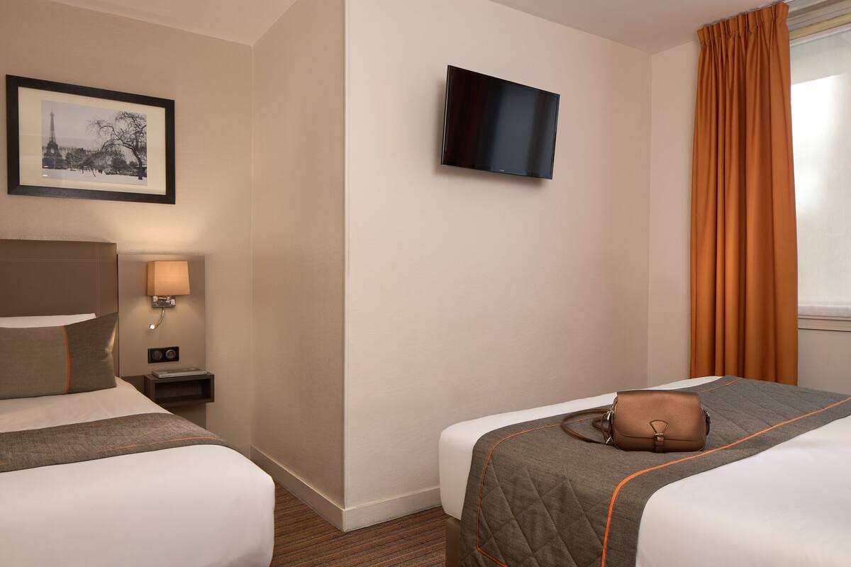 A hotel room with two beds, a flat-screen TV, a framed picture of the Eiffel Tower, a bedside lamp, and a brown handbag on one bed.
