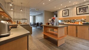 Une cuisine moderne équipée d’un grille-pain, d’un panier de fruits et d’une machine à café. On aperçoit à l’arrière-plan un coin repas avec des chaises et une table.