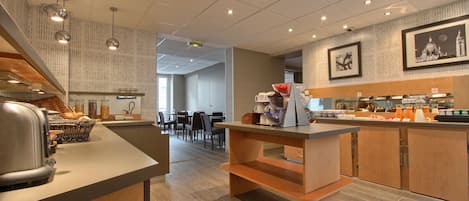 A modern kitchen with a toaster, a fruit bowl, and a coffee machine. There is a dining area with chairs and a table in the background.