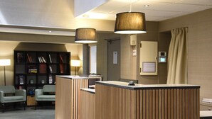 A reception desk with vertical wooden slats, two pendant lamps, a bookshelf, and a seating area with chairs. - Timhotel Opéra Madeleine (Paris)
