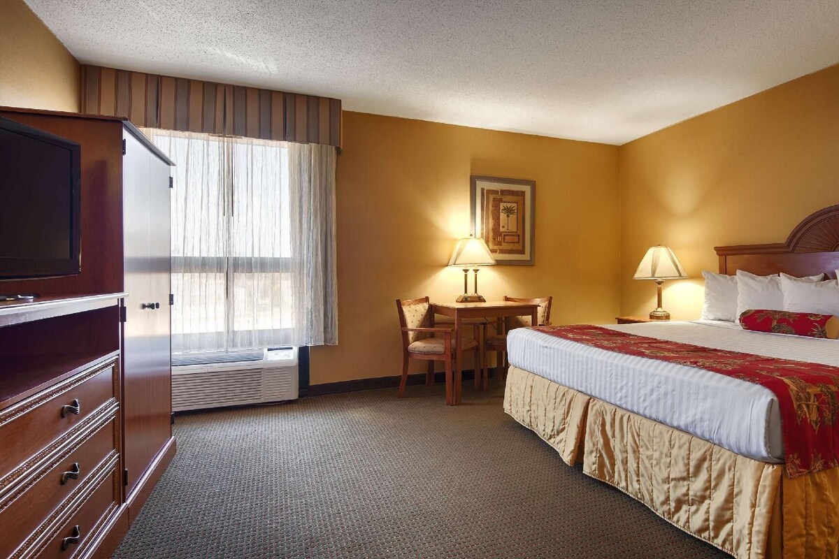 A hotel room with a bed, a desk with a chair, a television, and a window with curtains.