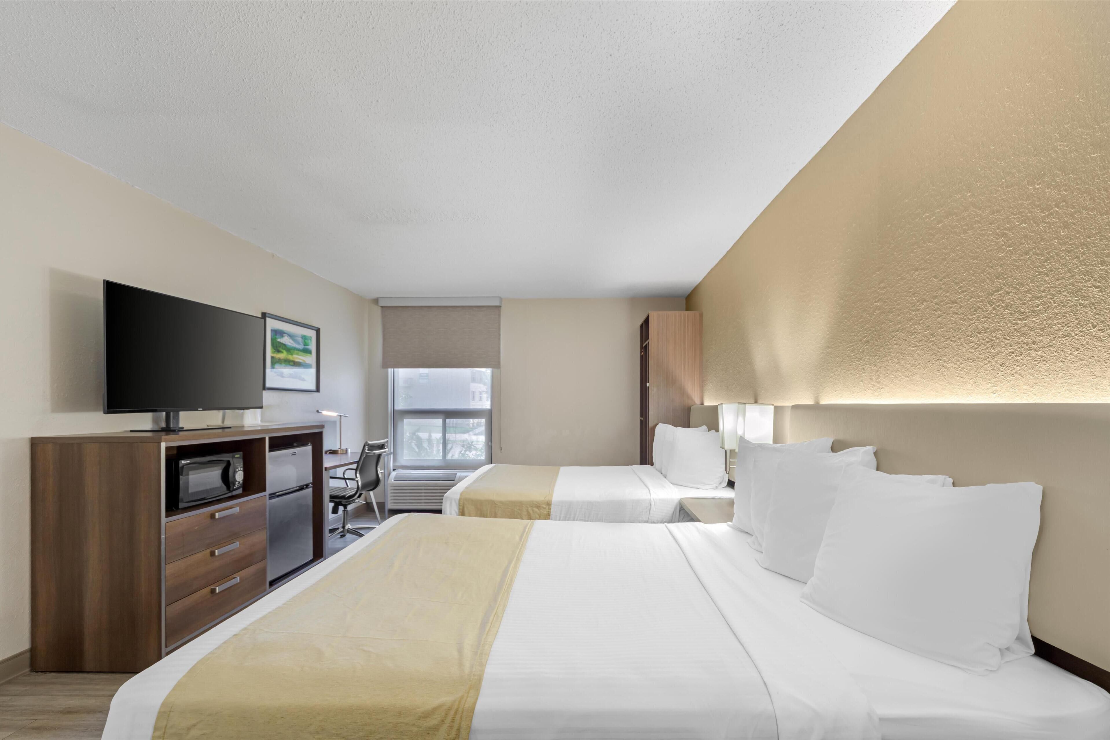 A hotel room with two beds, a TV, a desk with a chair, and a window.