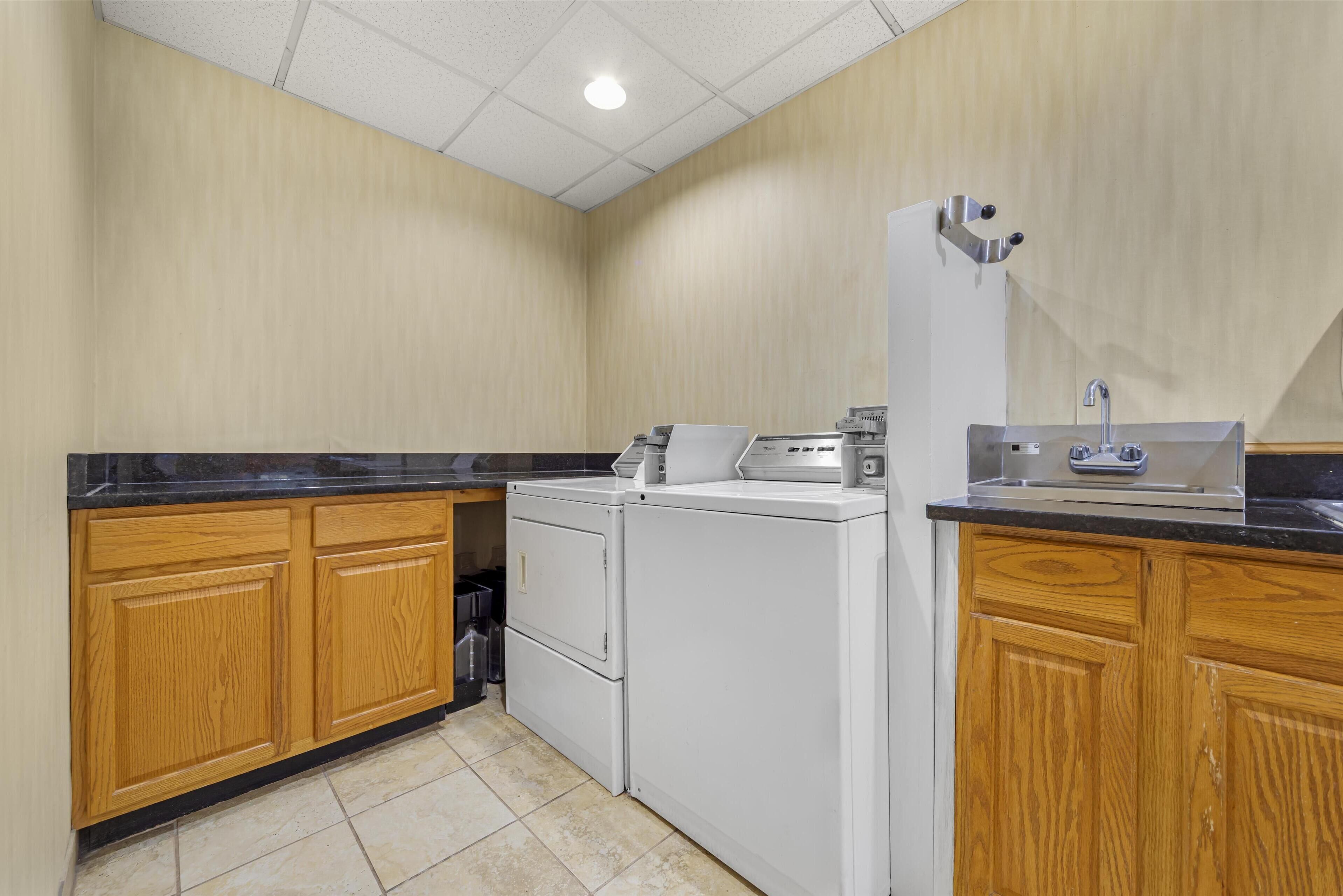 A laundry room with wooden cabinets, a washing machine, a dryer, and a sink.