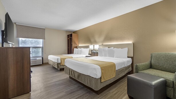 Quarto de hotel com duas camas, uma escrivaninha, uma cadeira e uma janela grande.