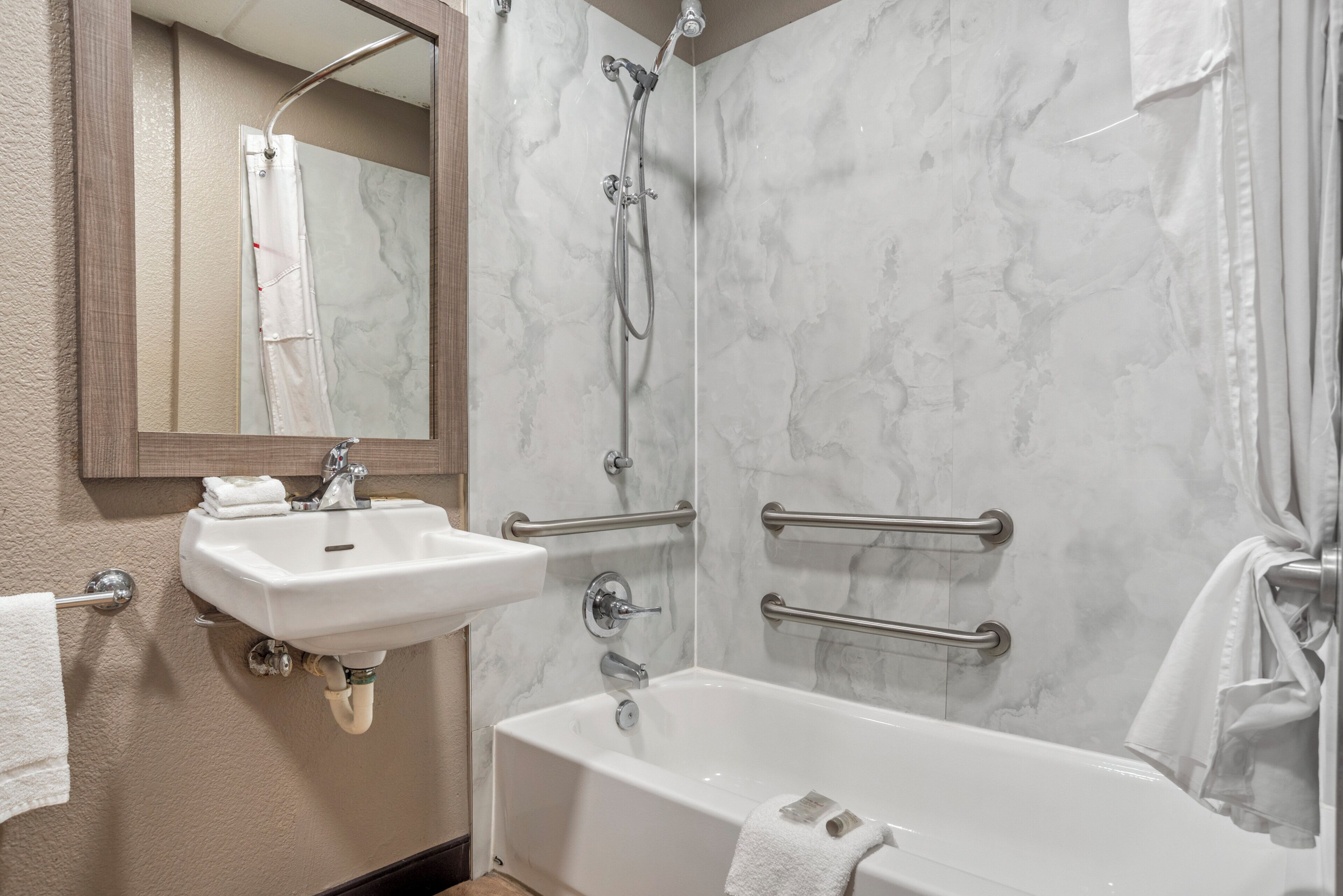A bathroom with a white bathtub, a sink, a shower with a handheld showerhead, and a mirror.
